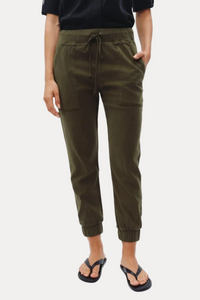 A person wearing olive green drawstring jogger pants with side pockets, paired with a black top and black flip-flop sandals, shown against a light gray studio background.