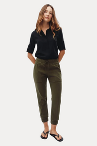 A woman modeling olive green drawstring cropped pants with a black shirt and black flip-flops, standing against a plain white studio background.