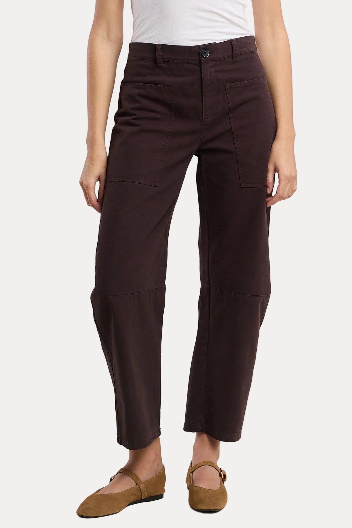 A model wearing dark brown cropped pants with a white top and brown flat shoes, shown from the waist down against a light beige background.