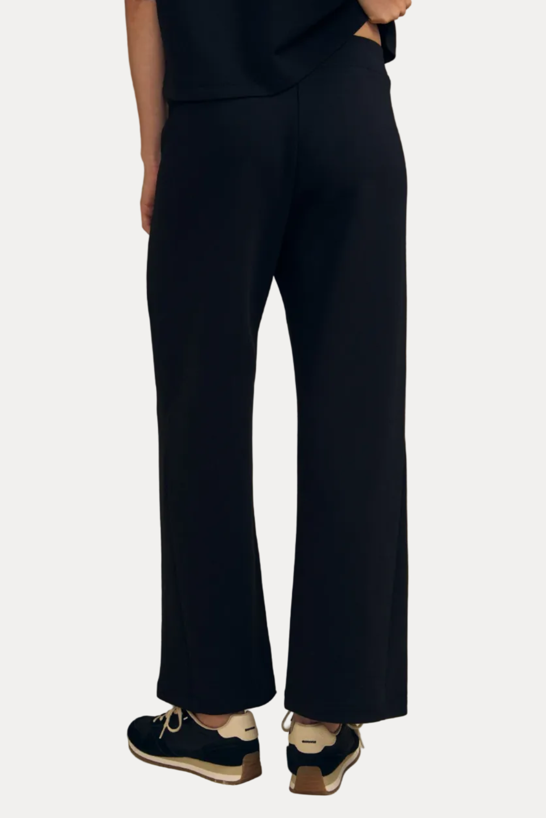 A person shown from the back wearing dark navy wide-leg trousers, a matching dark top, and navy sneakers against a plain beige studio background.