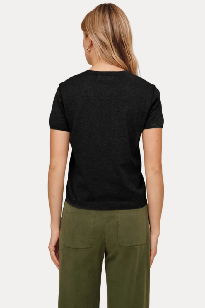 A woman shown from the back wearing a black short-sleeve crewneck t-shirt and olive green pants, set against a solid beige studio background.