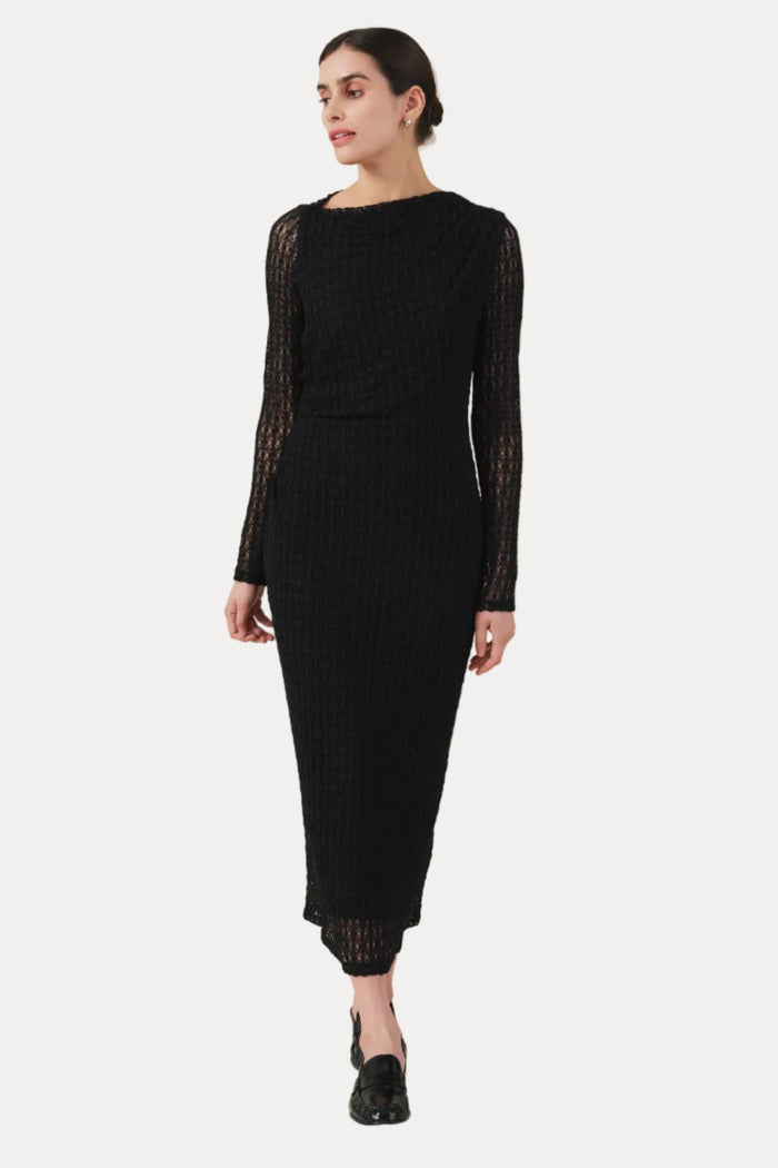 Woman wearing a black dress with sheer sleeves on a beige background