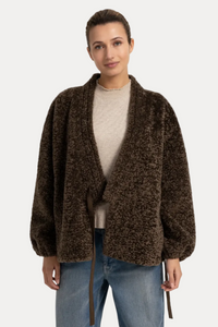 A woman modeling a brown textured, open-front fuzzy cardigan with a tie waist, worn over a beige top and blue jeans, against a plain white studio background.
