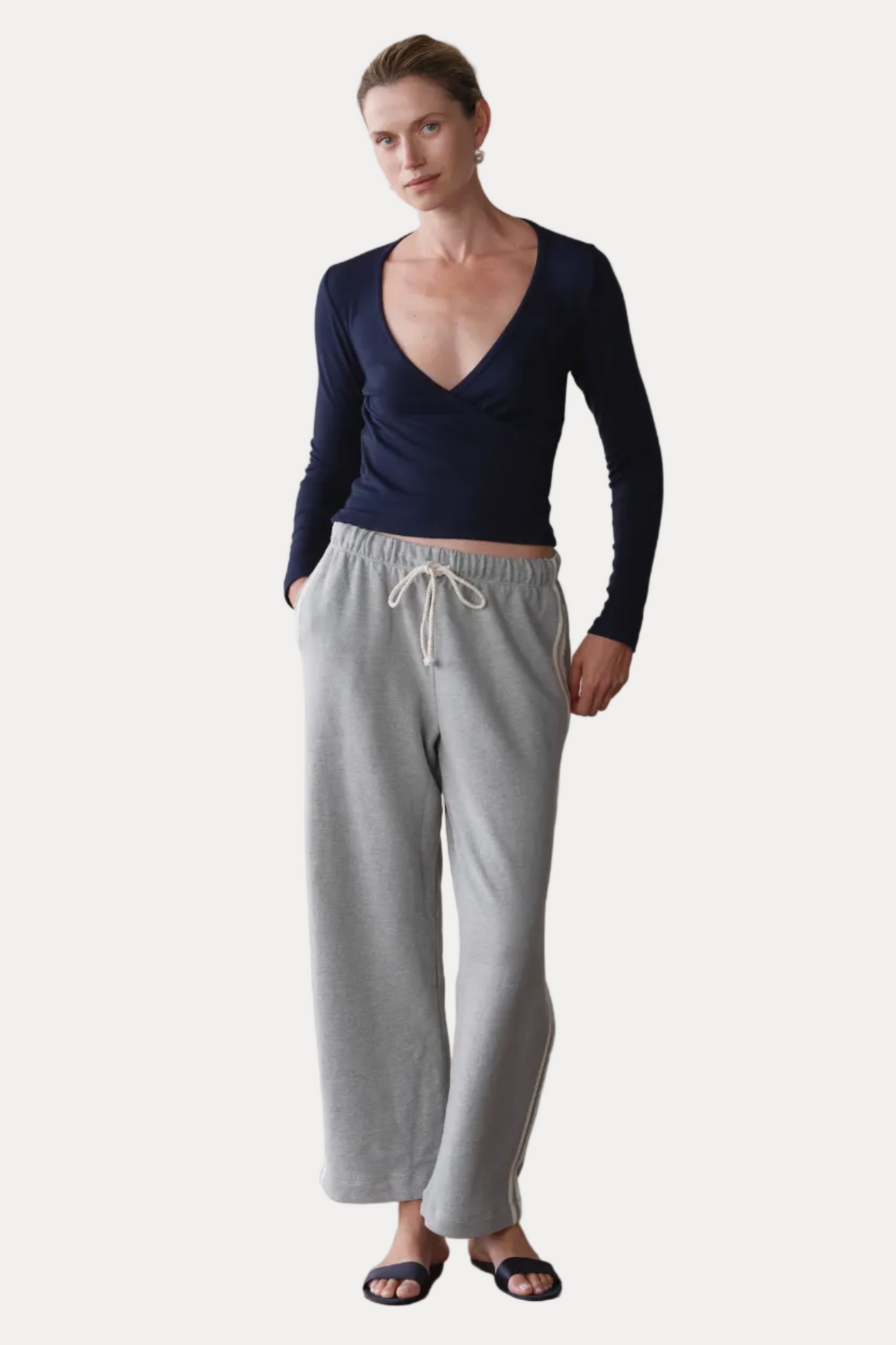 Woman wearing a navy long-sleeve top and gray sweatpants against a plain background