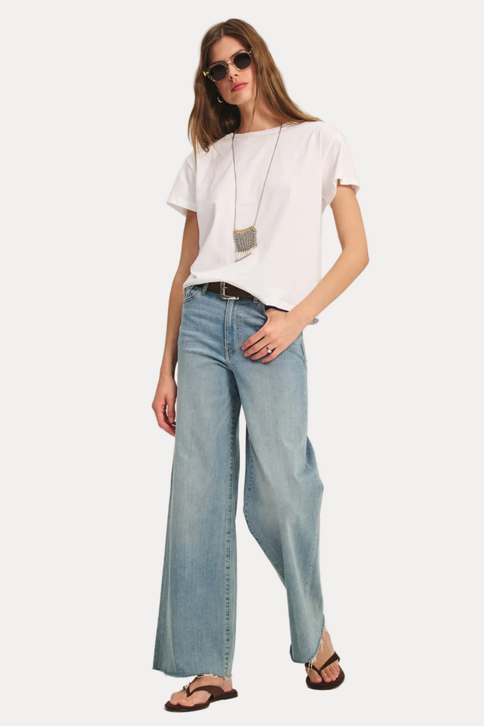 Woman wearing a white t-shirt and light blue jeans on a plain background